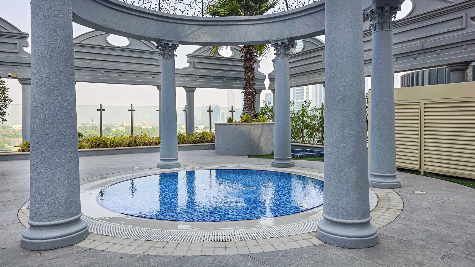 A circular pool with a tiled edge, surrounded by columns and a pergola structure.