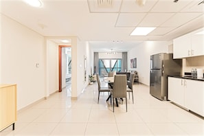 Eine moderne Küche mit einem Edelstahlkühlschrank, einem Essbereich mit Tisch und Stühlen sowie Blick ins Freie durch große Fenster.