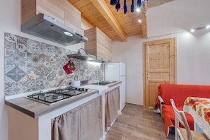 Eine kompakte Küche mit Gasherd, Backofen und Mikrowelle. Die Holzbalkendecke wird von einer Hängeleuchte erhellt.