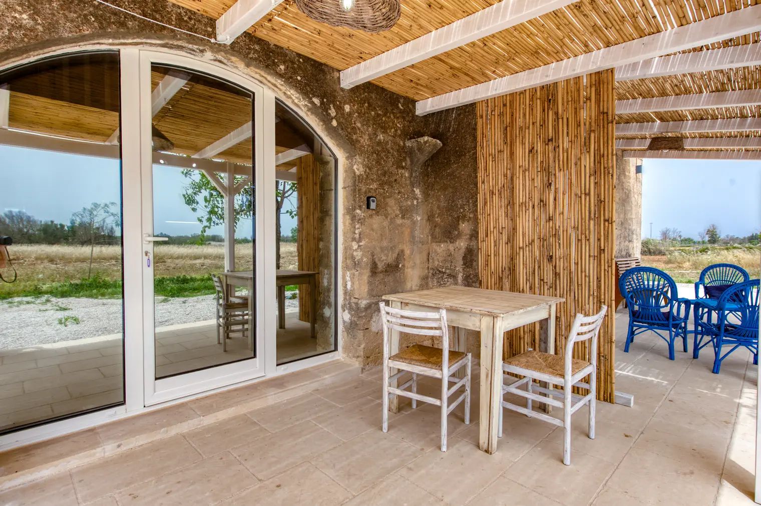 Ein Zimmer mit Glastür, Holztisch mit Stühlen und einer Bambuswand.