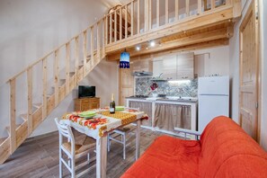 A compact kitchen with a wooden staircase, a dining table with a bottle of wine, and a sofa. - Room with Private Bathroom at Casolare Giardino Aiarella (Merine)