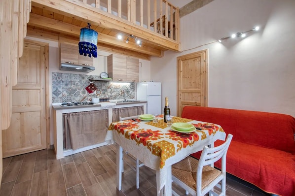A cozy kitchen with a dining table set for two, a red sofa, and a hanging blue lantern. - Room with Private Bathroom at Casolare Giardino Aiarella (Merine)