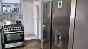 Una cocina con estufa, dos refrigeradores, un lavamanos y un letrero de salida de emergencia.