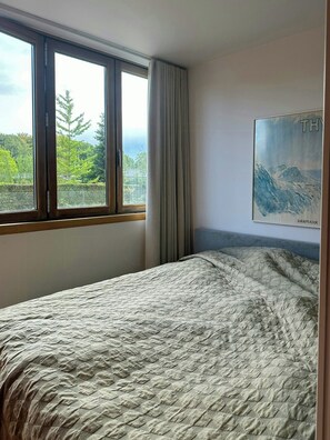 Une chambre à coucher avec un lit, une fenêtre et un tableau représentant un paysage.