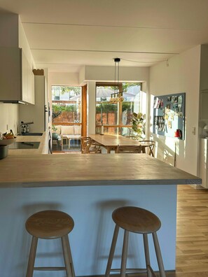A modern kitchen with a central island, bar stools, and a dining area with a view of the outdoors. - Spacious flat by Amager Fælled and the harbour (København)