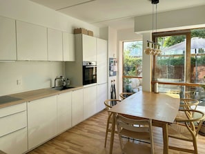 Une cuisine moderne avec des meubles blancs, un plan de travail en bois et un coin repas comprenant une table et des chaises.