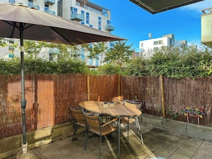 Une terrasse extérieure avec une table et des chaises, une clôture en bois et des bâtiments en arrière-plan.