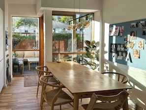 A dining area with a wooden table and chairs, large windows, and a wall with photos. - Spacious flat by Amager Fælled and the harbour (København)