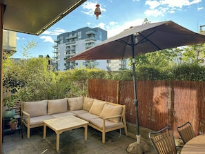 An outdoor patio with a sofa, table, and chairs, a wooden fence, and a building in the background. - Spacious flat by Amager Fælled and the harbour (København)