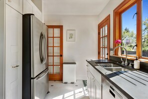 A kitchen with a refrigerator, a sink, and a window with a view of greenery. - Spacious 5-bedroom house with AC, hot tub and space to spread out (Seattle)
