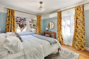 A bedroom with a large bed, a bedside table, a mirror, and a window with curtains. - Spacious 5-bedroom house with AC, hot tub and space to spread out (Seattle)