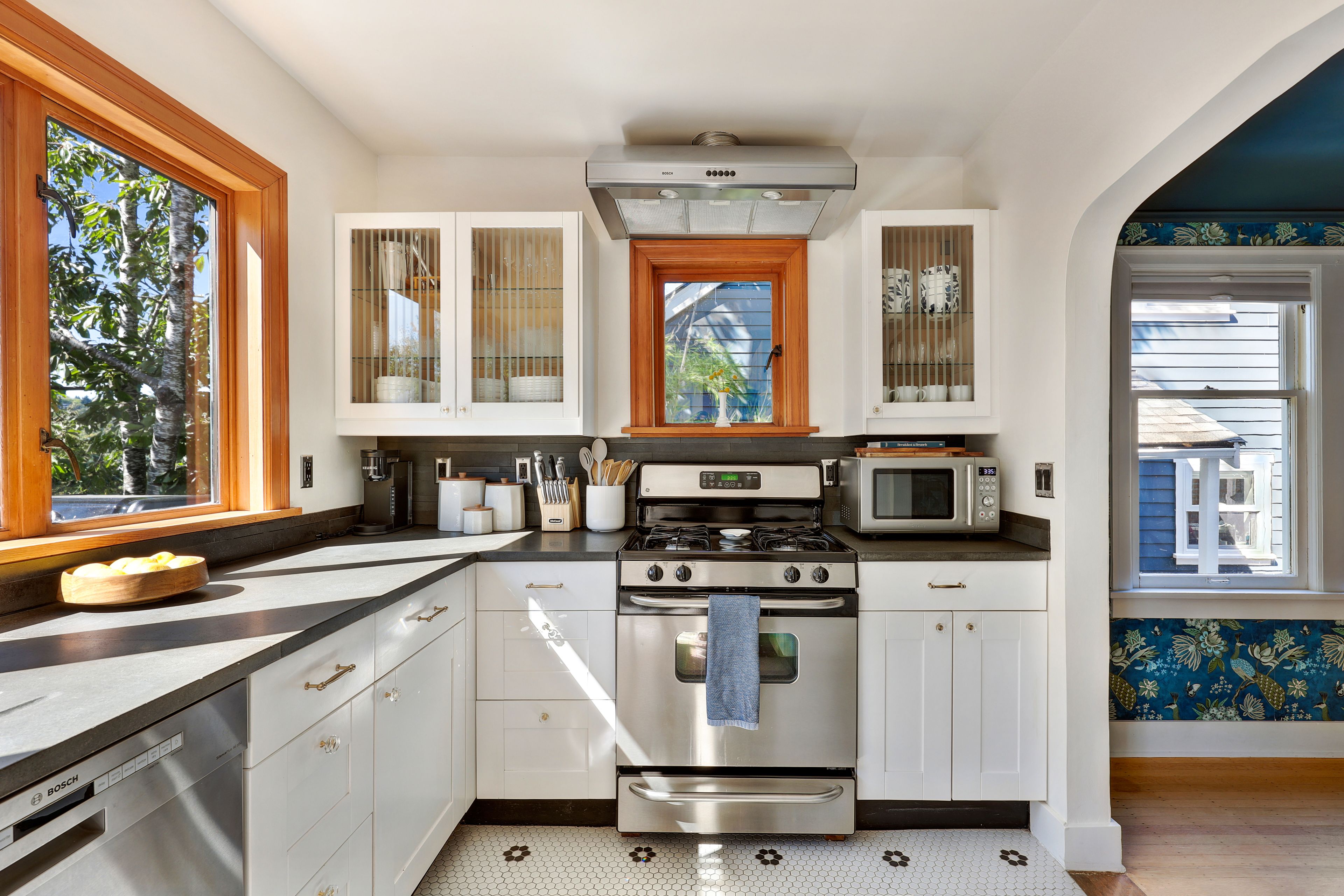 A modern kitchen with white cabinetry, a Bosch range, a microwave, and a window with a view of trees.