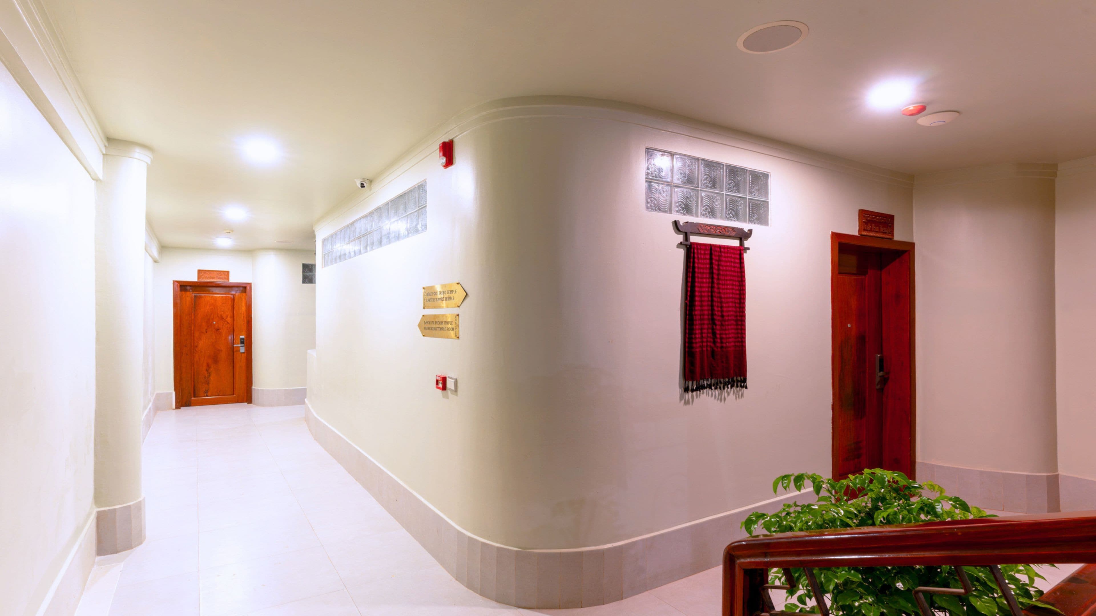 Un pasillo con una pared curva, una puerta roja y una planta.