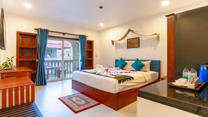 Habitación de hotel con cama, escritorio, silla, balcón y zona de ducha.