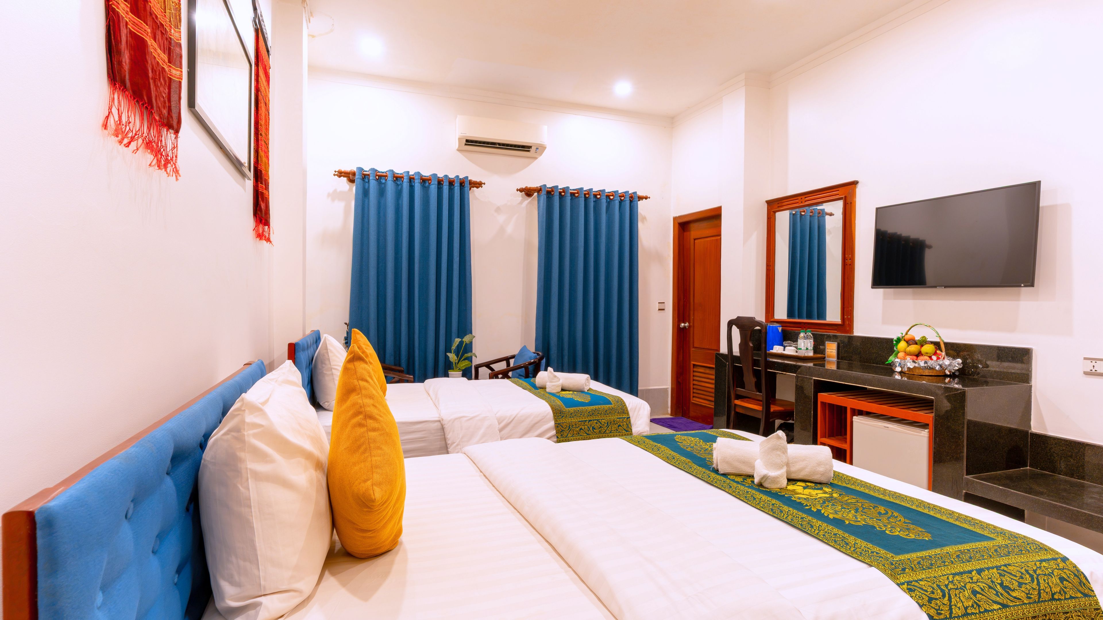 A hotel room with two beds, a desk, a TV, and a bathroom.