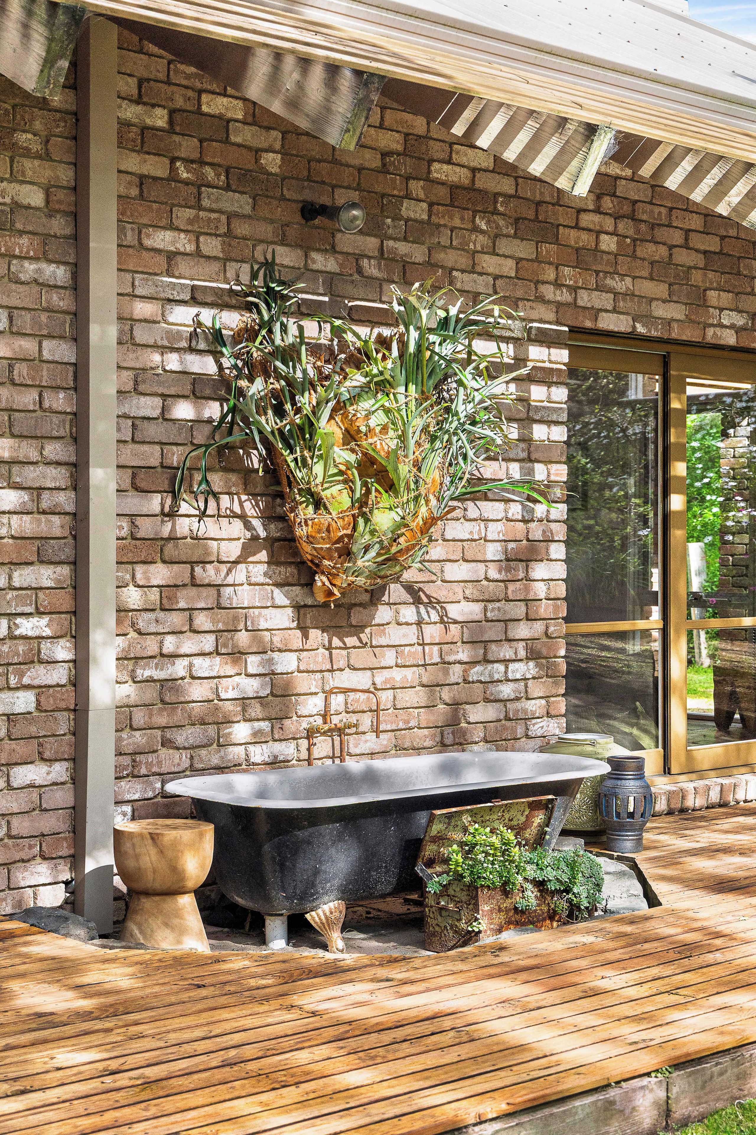A brick wall with a hanging plant, a black bathtub, and a wooden deck.