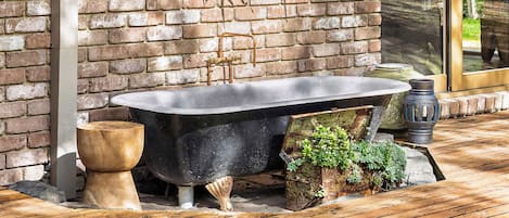 A brick wall with a hanging plant, a black bathtub, and a wooden deck.