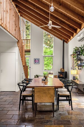 A spacious dining area with a long wooden table, multiple chairs, and a ceiling fan. - The Stillhouse | Sauna, Soak & Pet-Friendly Escape (Rye)