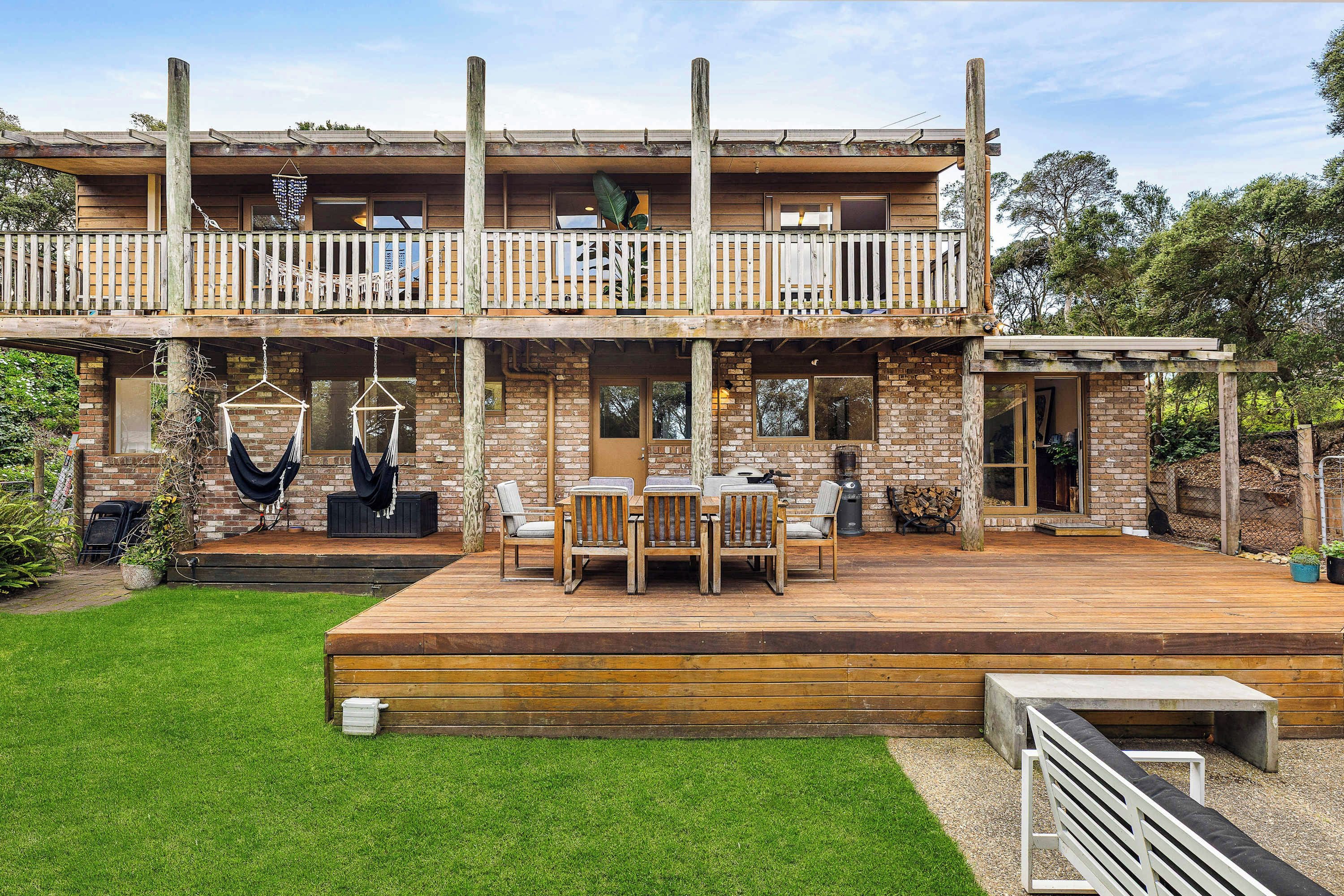 A two-story wooden house with a balcony, outdoor seating area, and a well-maintained lawn.