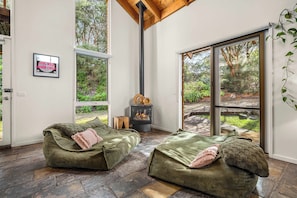 A cozy room with a fireplace, two green sofas, and a large window offering a view of the outdoors. - The Stillhouse | Sauna, Soak & Pet-Friendly Escape (Rye)