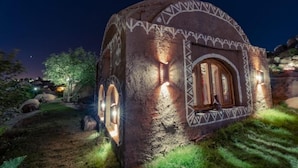A stone building with a window and a door, surrounded by grass and rocks. - Krouma Camp & Ecolodge (Aswan)