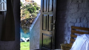 A room with a bed, a wooden headboard, a window with a view of a rocky landscape, and a door leading outside. - Krouma Camp & Ecolodge (Aswan)