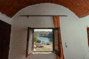 Una habitación con ventana que da a un río, un arco de ladrillo y una cortina.