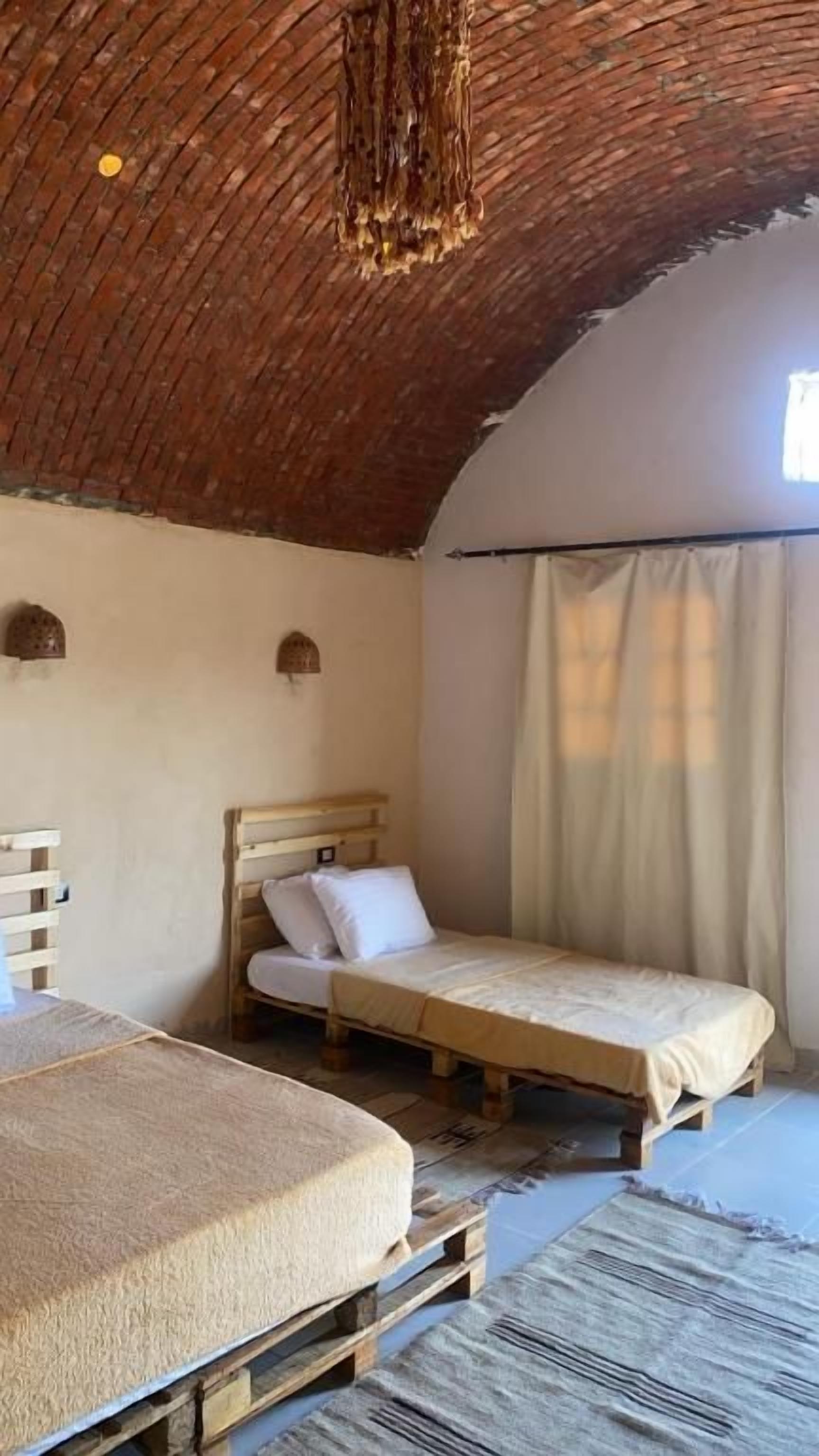 A rustic room with a sloped ceiling, two wooden beds, a small table, and a window with curtains.