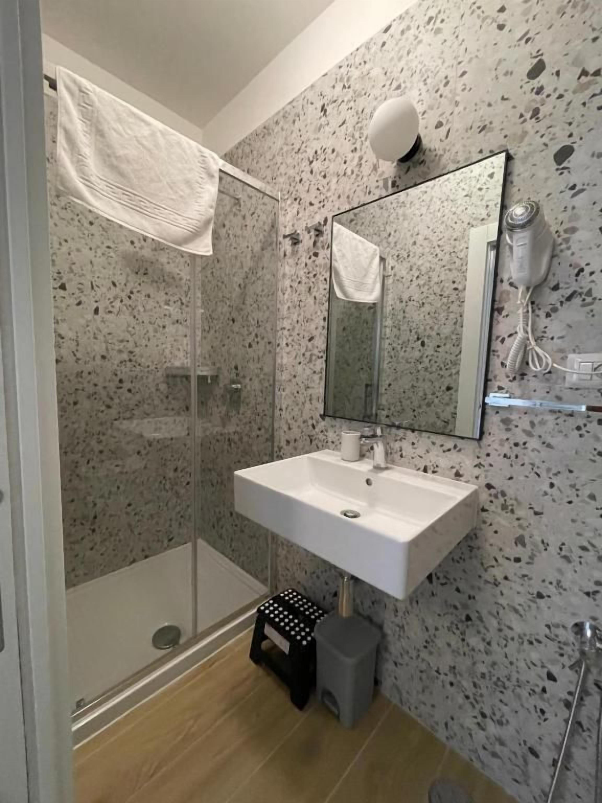 Un baño con cabina de ducha de vidrio, un lavabo blanco, un espejo y una toalla colgada en la pared.