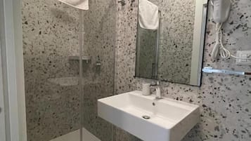 Un baño con cabina de ducha de vidrio, un lavabo blanco, un espejo y una toalla colgada en la pared.