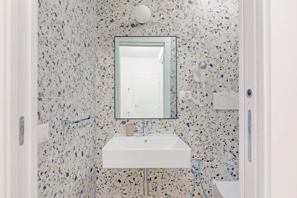 Casa de banho com lavatório branco, espelho e parede com padrão salpicado.