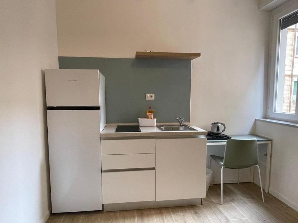 Une cuisine compacte équipée d’un réfrigérateur, d’un évier et d’un petit coin repas avec une chaise.