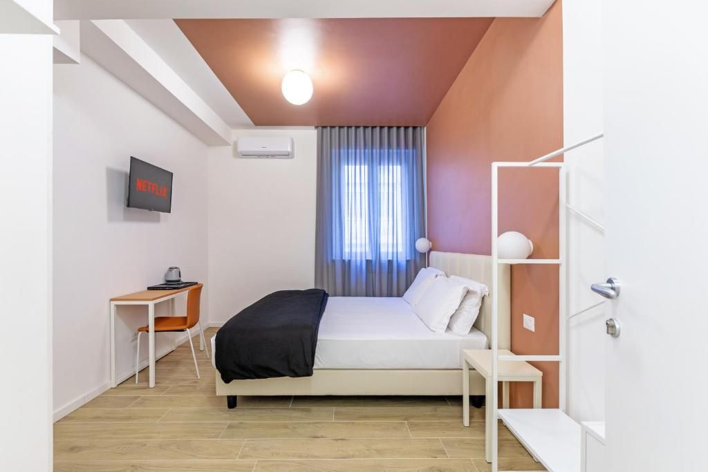 Un dormitorio con cama, escritorio, televisor y ventana con cortinas.