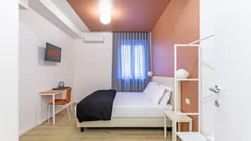 Un dormitorio con cama, escritorio, televisor y ventana con cortinas.