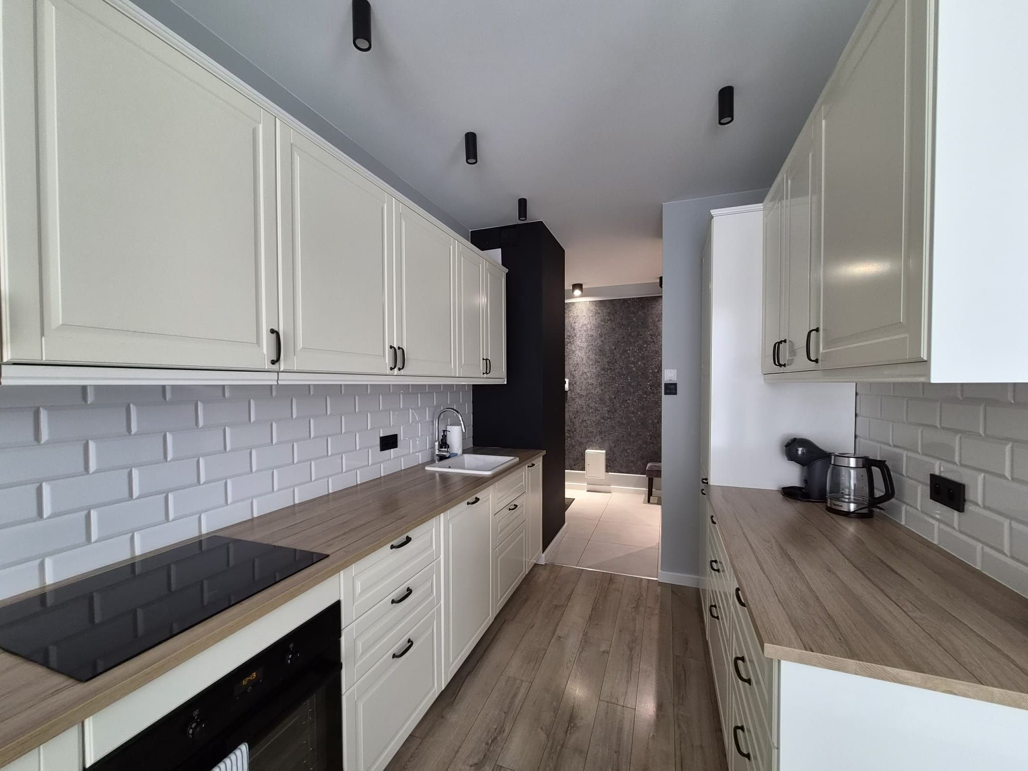 A modern kitchen with white cabinets, a black backsplash, and wooden countertops.
