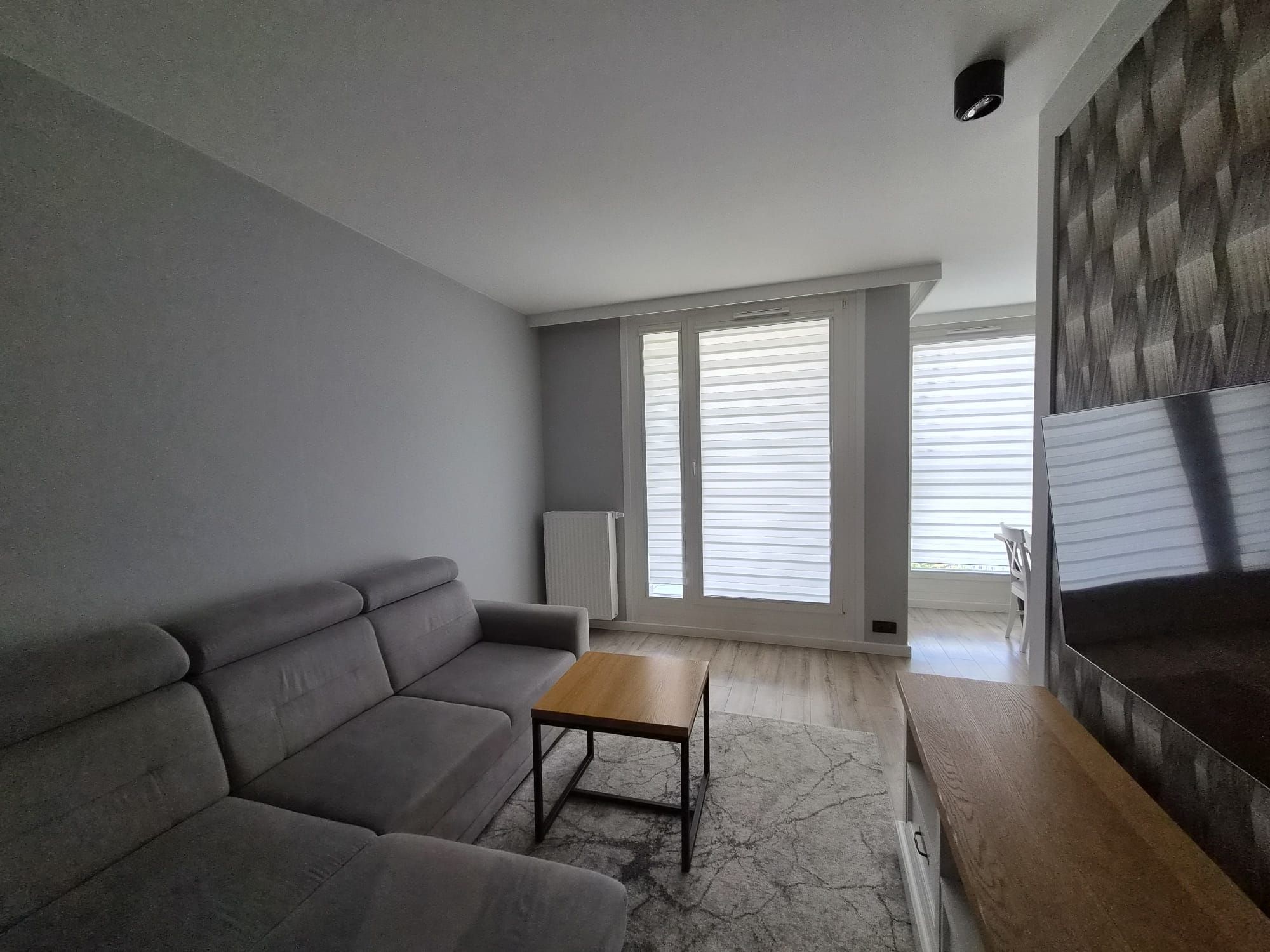 Una sala de estar moderna con un sofá gris, una mesa de centro de madera y un amplio ventanal con persianas.