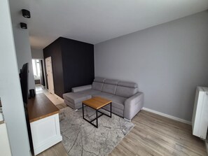 Ein modernes Wohnzimmer mit einem grauen Ecksofa, einem Holztisch und einem grauen Teppich.