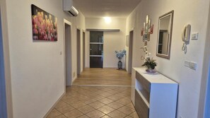 A hallway with a tiled floor, a reception desk, a vase with flowers, and a painting on the wall. - Meneghin House Apartment with Wi-Fi and Air Conditioning (San Zenone degli Ezzelini)