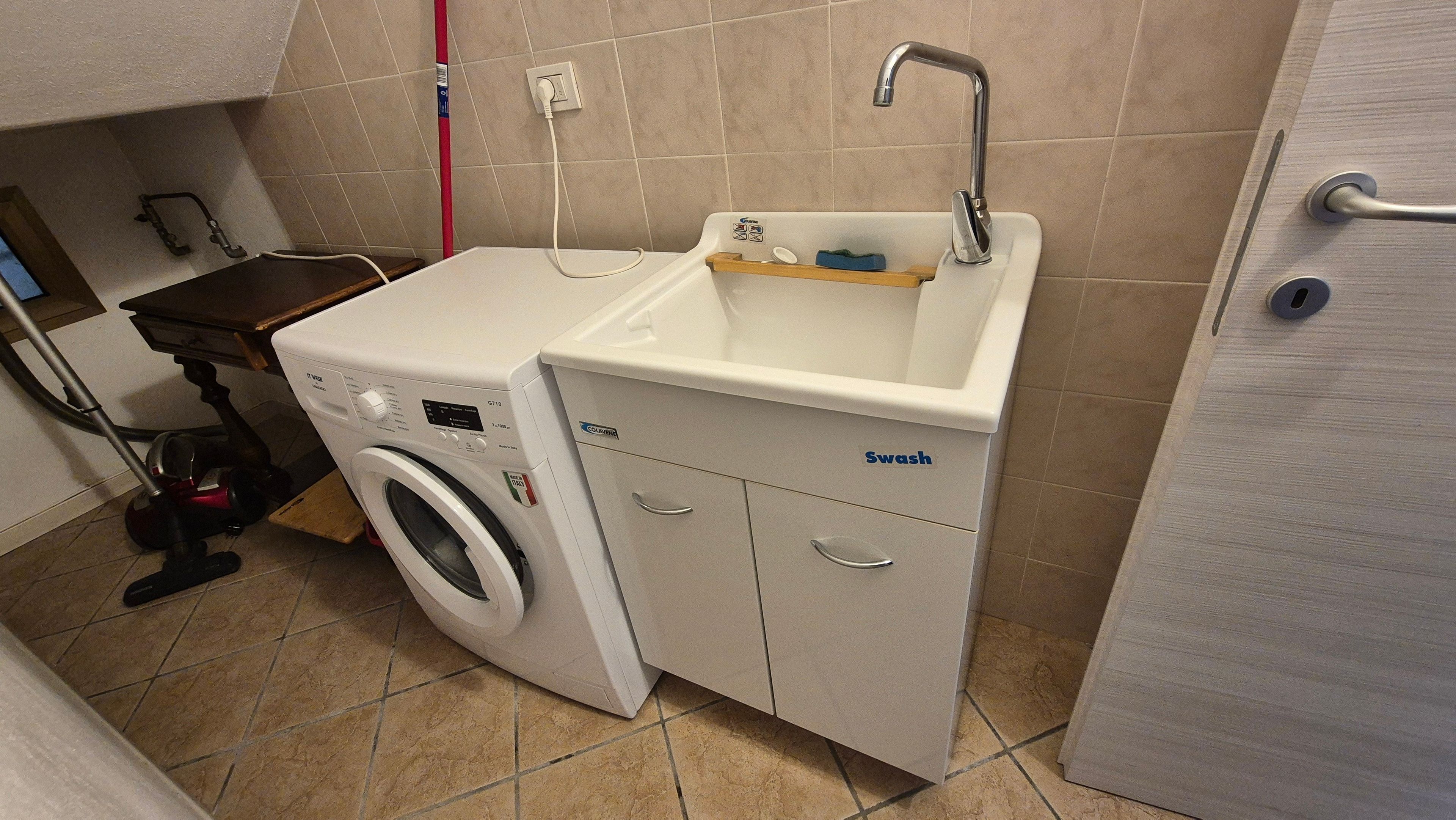 A compact laundry area with a washing machine, a sink, and storage cabinets.