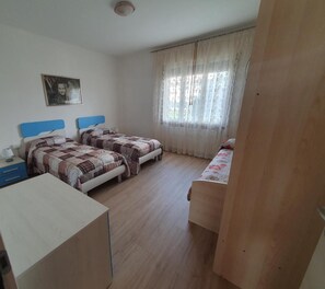 Ein Schlafzimmer mit zwei Betten, einem Schreibtisch und einem Fenster mit Vorhängen.