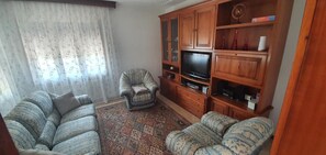 Ein Wohnzimmer mit einer Sofagarnitur, einem Fernseher, Holzschränken und einem gemusterten Teppich.