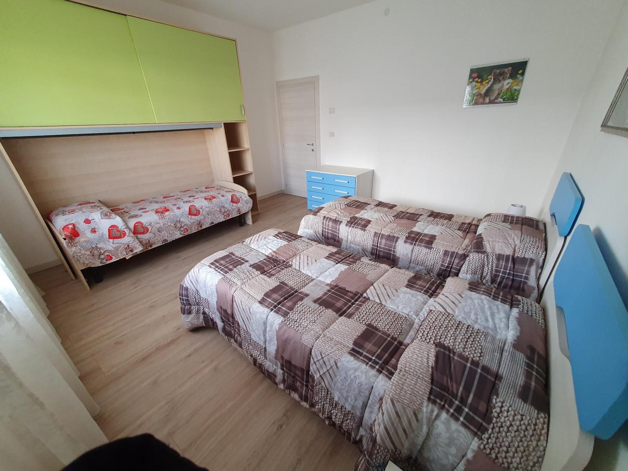 Ein Zimmer mit zwei Betten, einem grünen Schrank, einer blauen Kommode und einer Tür.