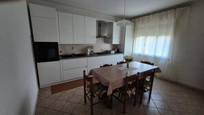 A compact kitchen with white cabinets, a black oven, and a dining table with chairs. - Meneghin House Apartment with Wi-Fi and Air Conditioning (San Zenone degli Ezzelini)