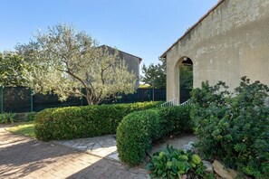 A courtyard with a paved walkway, a building with an arched entrance, and a tree with sparse leaves. - Comfortable House with Garden, Wi-Fi, and Air Conditioning in Saint-Gilles (Saint-Gilles)