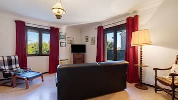 Een woonkamer met een bank, een fauteuil, een televisie en een lamp.
