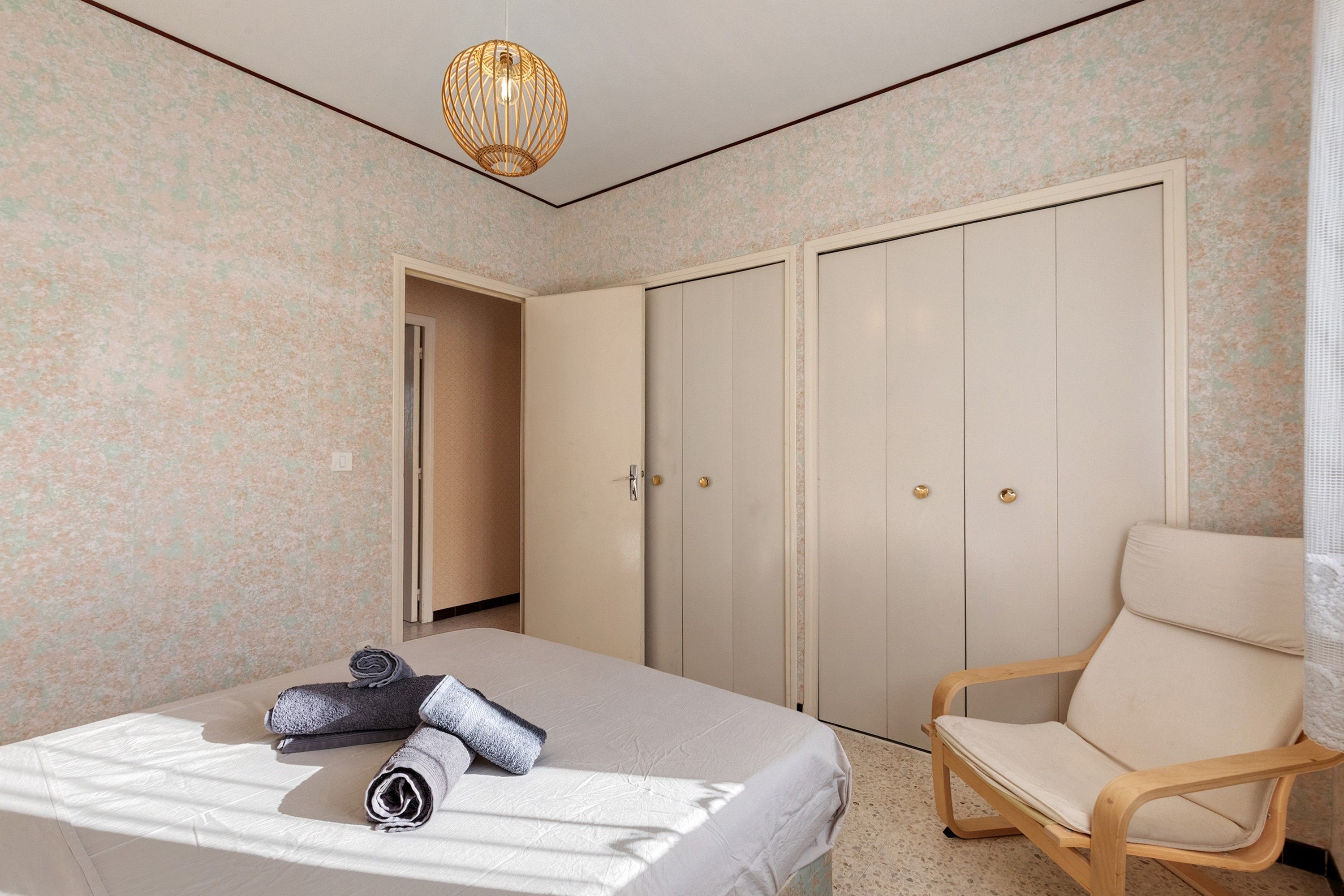 Een slaapkamer met een bed, een stoel, een kledingkast en een hanglamp.