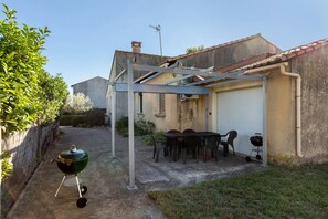 A covered outdoor patio with a table and chairs, a barbecue grill, and a garage door.