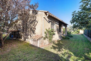 A rustic building with a tiled roof, a small porch, and a grassy yard.