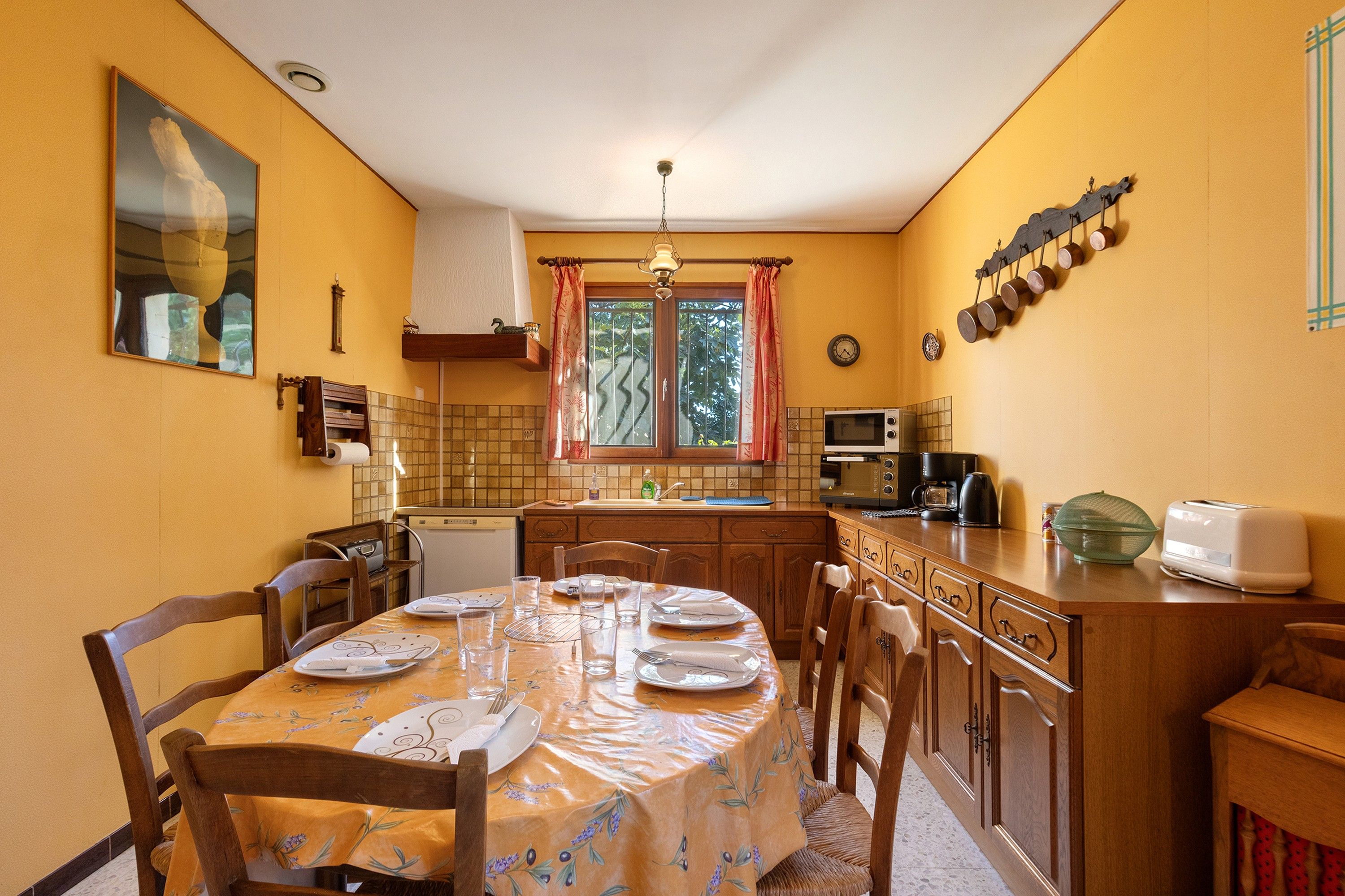 Une cuisine compacte avec un coin repas, équipée d’appareils électroménagers de base et d’une fenêtre avec des rideaux.
