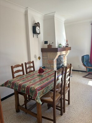 Un coin repas avec une table dressée pour quatre personnes, une cheminée et une horloge au mur.
